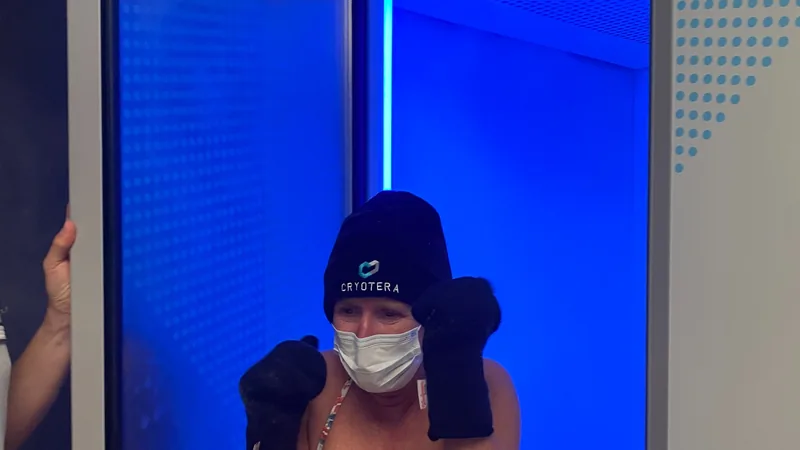 Une cliente équipée d'un bonnet et de moufles de protection à l'entrée de la cabine de cryothérapie Cryotera.
