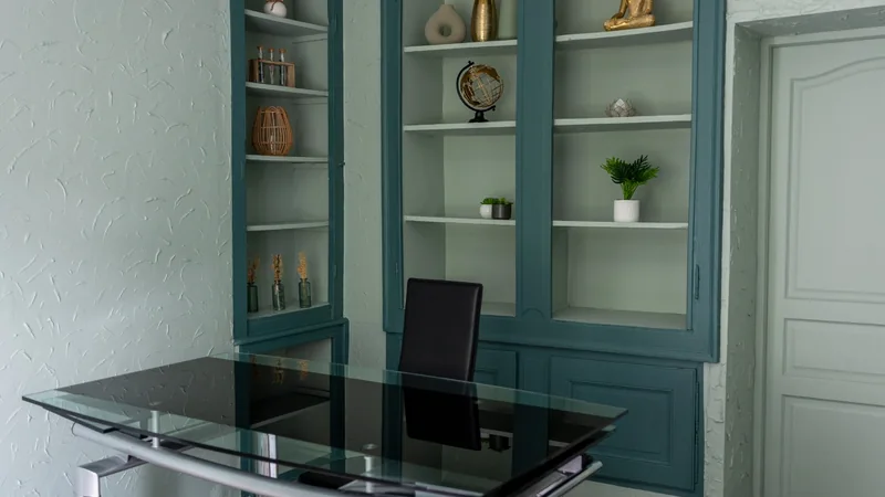 Bureau professionnel avec table en verre et bibliothèques intégrées aux boiseries vertes dans le cabinet d'avocate rénové.
 Copier l'alt