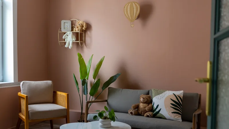 Salle d'attente du cabinet d'avocate rénové à Marchiennes avec mur rose poudré, canapé, fauteuil et peluches pour accueillir les familles.